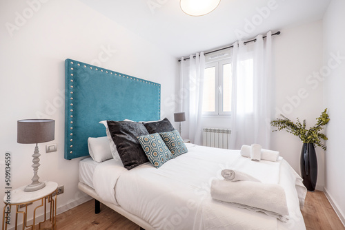 Double bedroom with beautiful white decoration with black and blue cushions  headboard upholstered in blue velvet fabric and light wood floors