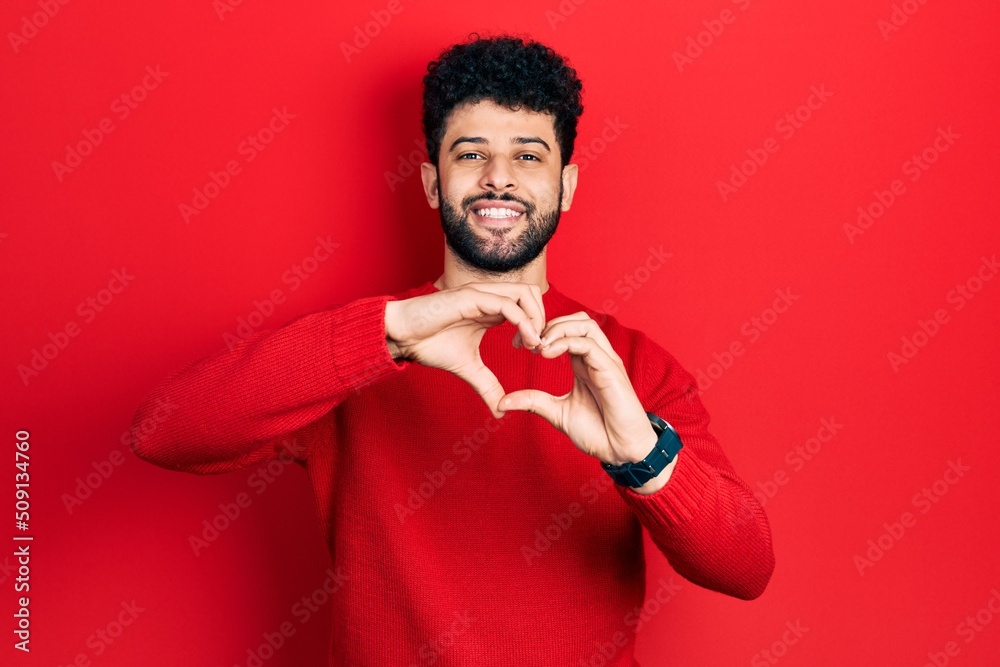 Young arab man with beard wearing casual red sweater smiling in love doing heart symbol shape with hands. romantic concept. Young arab man with beard wearing casual red sweater smiling in love doing heart symbol shape with hands. romantic concept.
