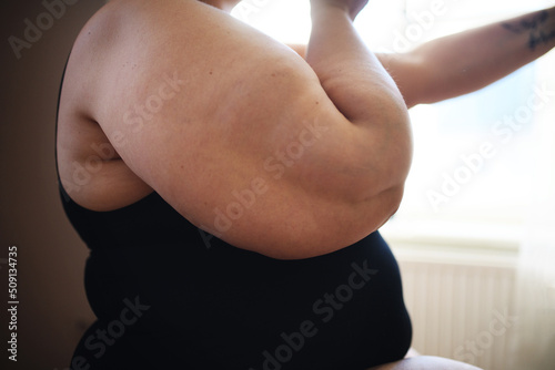 Close up for woman obese body, standing and looking through the window at home. photo