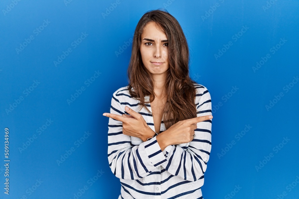 Young hispanic woman standing over blue isolated background pointing to both sides with fingers, different direction disagree Young hispanic woman standing over blue isolated background pointing to both sides with fingers, different direction disagree