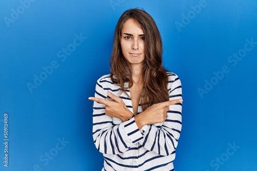 Young hispanic woman standing over blue isolated background pointing to both sides with fingers, different direction disagree © Krakenimages.com