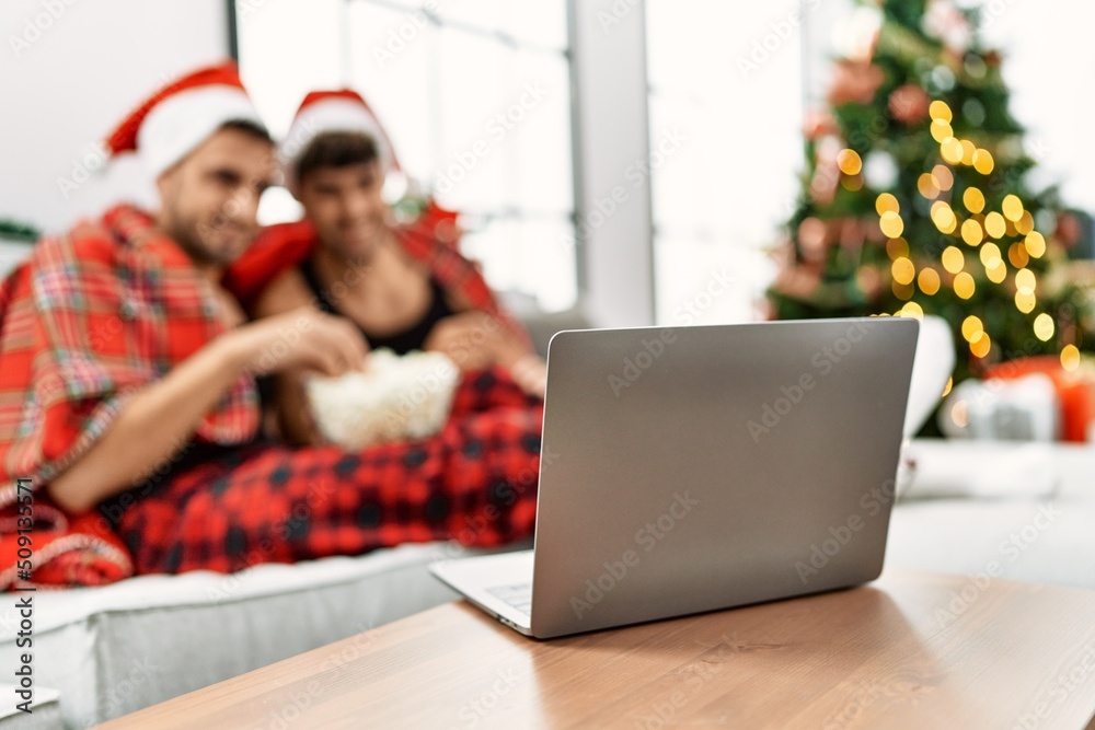 Two hispanic men couple watching movie sitting by christmas tree at home Two hispanic men couple watching movie sitting by christmas tree at home