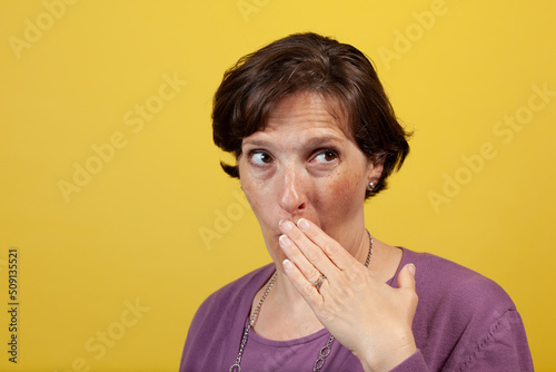 Fotografie Attractive mature woman in purple blouse on a yellow background with hand over m