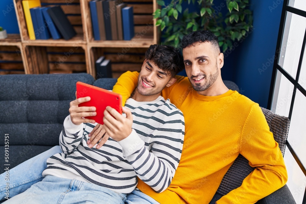 Two man couple using touchpad sitting on sofa at home Two man couple using touchpad sitting on sofa at home