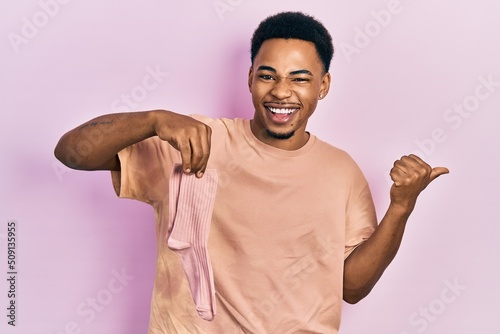 Young african american man holding socks pointing thumb up to the side smiling happy with open mouth
