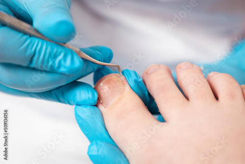 Fototapeta Naklejka Na Ścianę i Meble -  A chiropodist does a pedicure for the client's feet, cleaning the nails with a double-sided curette. Close up, top view. The concept of salon professional nail care and chiropody