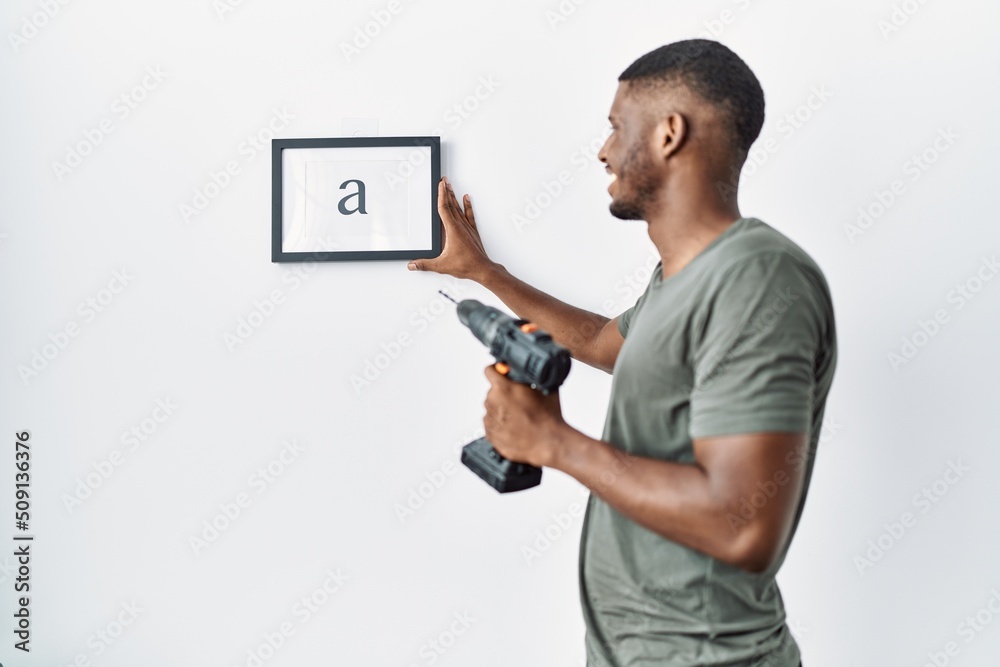 Young african american man hanging frame using drill at home Young african american man hanging frame using drill at home