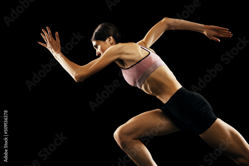 Studio shot of young muscular woman running isolated on black background. Sport, track-and-field athletics, competition and active lifestyle concept