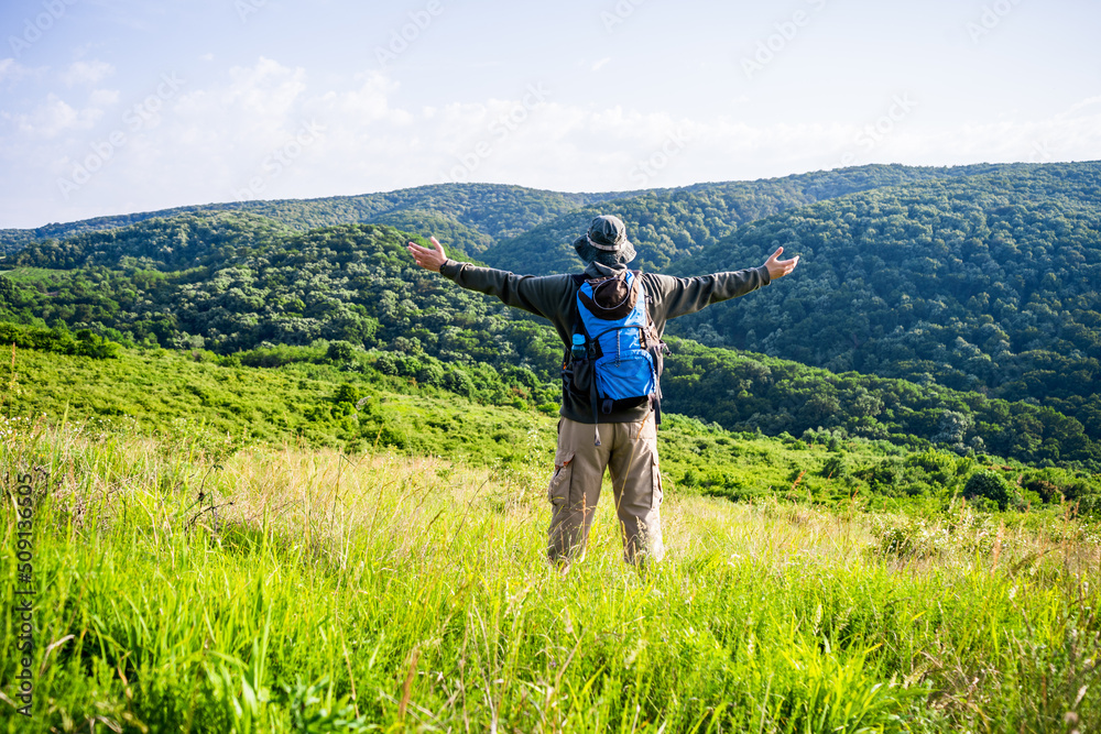 Man hiker with arms raised enjoys in beautiful view in the nature.	