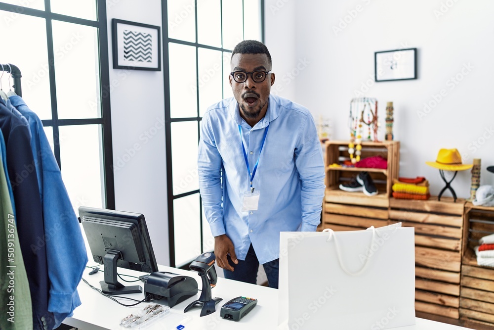 Young african man working as manager at retail boutique afraid and shocked with surprise and amazed expression, fear and excited face. Young african man working as manager at retail boutique afraid and shocked with surprise and amazed expression, fear and excited face.