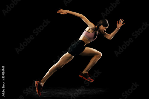 Studio shot of young muscular woman running isolated on black background. Sport, track-and-field athletics, competition and active lifestyle concept