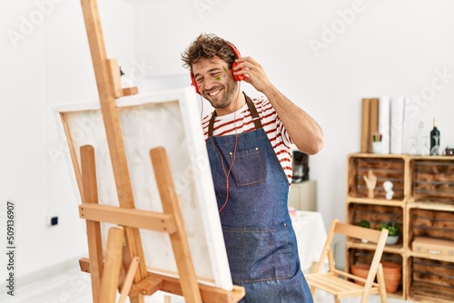 Young hispanic man smiling confident drawing and listening to music at art studio