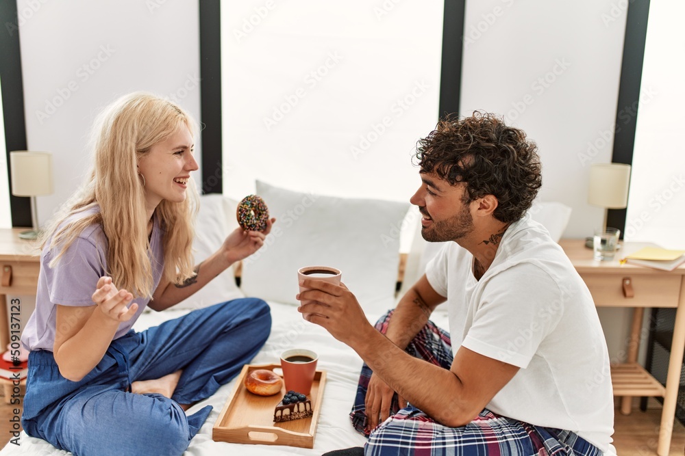 Young beautiful couple smiling happy having breakfast on the bed at home.