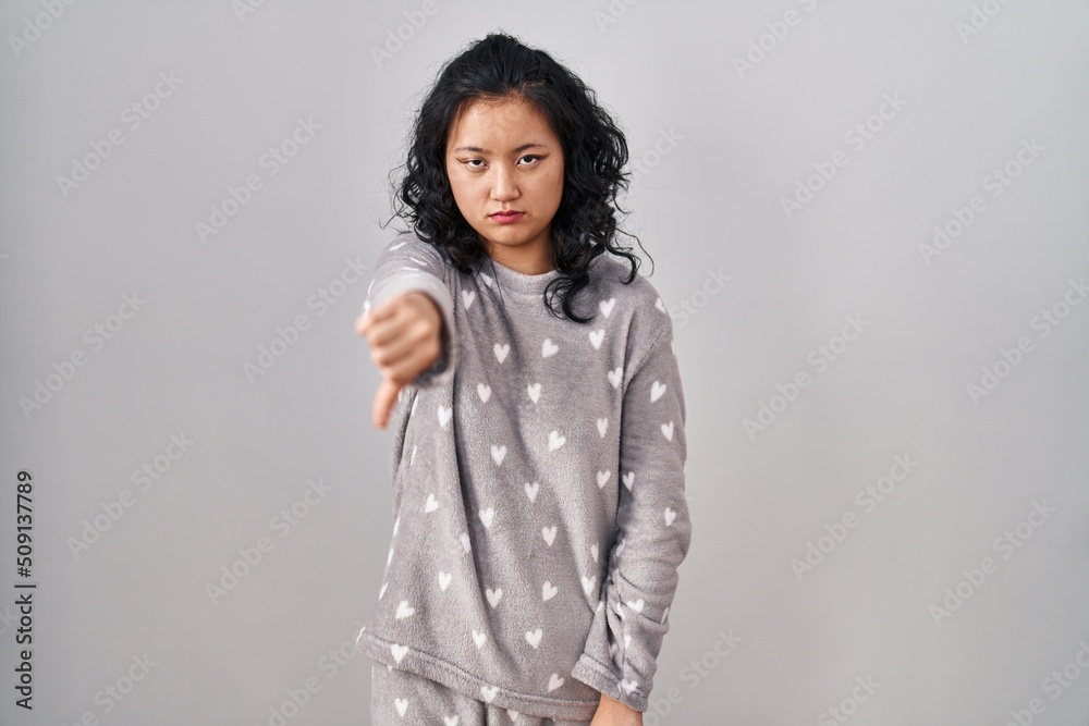 Young asian woman wearing pajama looking unhappy and angry showing rejection and negative with thumbs down gesture. bad expression. Young asian woman wearing pajama looking unhappy and angry showing rejection and negative with thumbs down gesture. bad expression.