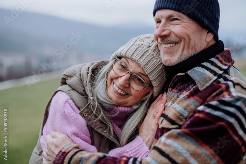 Senior man hugging and consoling his wife outdoors in garden in winter.