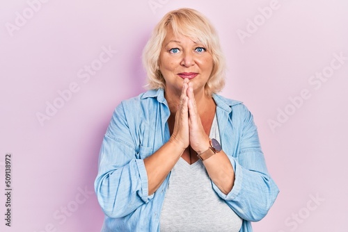 Middle age blonde woman wearing casual clothes begging and praying with hands together with hope expression on face very emotional and worried. begging.