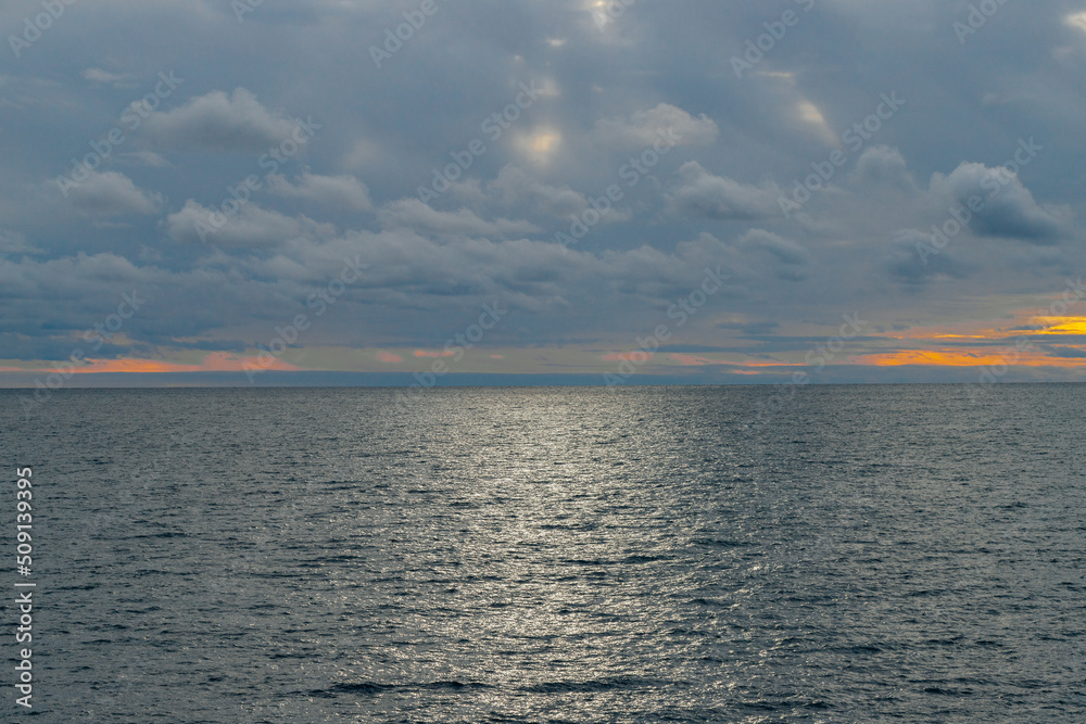 Obraz premium Calm sea and blue sky with white cirrus clouds. The sun shines through the clouds.