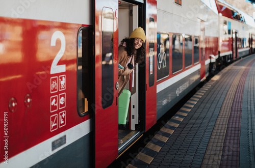 Happy young traveler woman with luggage getting off the train at train station platform photo