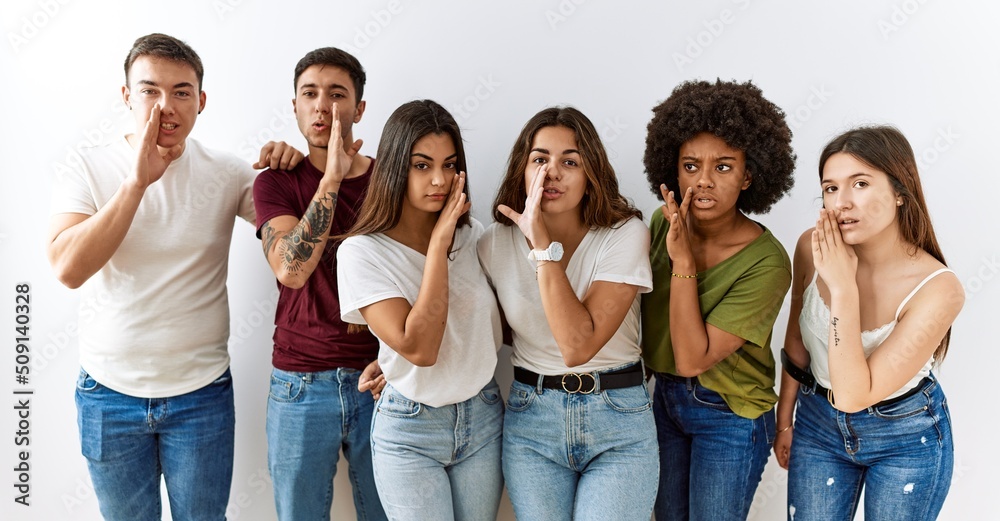 Fototapeta premium Group of young friends standing together over isolated background hand on mouth telling secret rumor, whispering malicious talk conversation