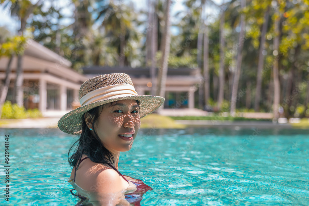 Happy asian woman in red swimsuit and a straw hat relaxing in swimming pool looking at camera by the pool at Koh Mak, Phangnga, Thailand. relax and travel concept. Comfort resort summer vacation