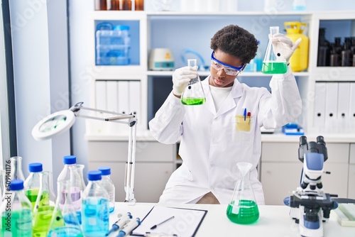 African american woman wearing scientist uniform measuring liquid at laboratory