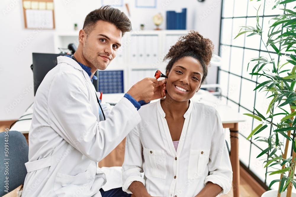 Man and woman wearing doctor uniform examining ear using otoscope at clinic Man and woman wearing doctor uniform examining ear using otoscope at clinic