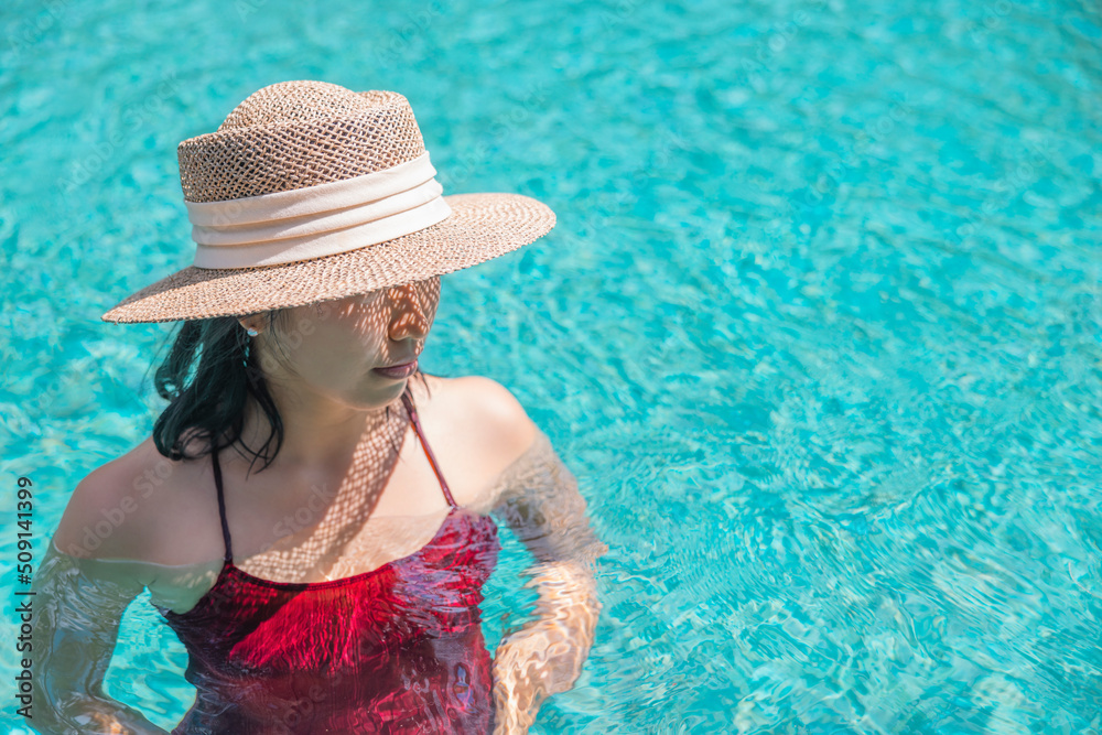 Happy asian woman in red swimsuit and a straw hat relaxing in swimming pool looking at view by the pool at Koh Mak, Phangnga, Thailand. relax and travel concept. Comfort resort summer vacation
