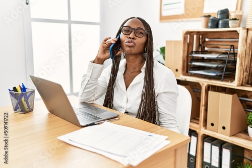 Black woman with braids working at the office speaking on the phone looking at the camera blowing a kiss on air being lovely and sexy. love expression.