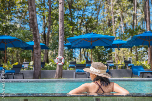 Happy asian woman in red swimsuit and a straw hat relaxing in swimming pool looking at view by the pool at Koh Mak, Phangnga, Thailand. relax and travel concept. Comfort resort summer vacation © TripleP Studio