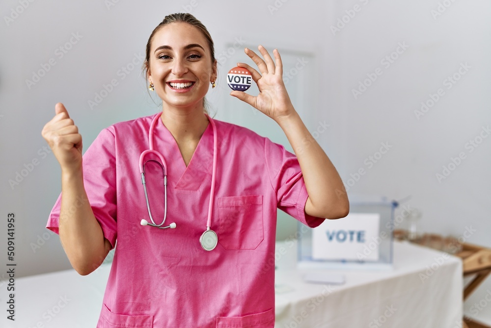 Young nurse woman at political campaign holding usa vote badge screaming proud, celebrating victory and success very excited with raised arms Young nurse woman at political campaign holding usa vote badge screaming proud, celebrating victory and success very excited with raised arms