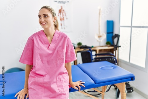 Young blonde woman wearing physiotherapist uniform working at physiotherapy clinic