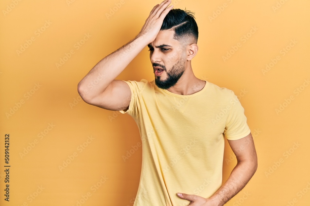 Handsome man with beard wearing casual yellow t shirt surprised with hand on head for mistake, remember error. forgot, bad memory concept. Handsome man with beard wearing casual yellow t shirt surprised with hand on head for mistake, remember error. forgot, bad memory concept.