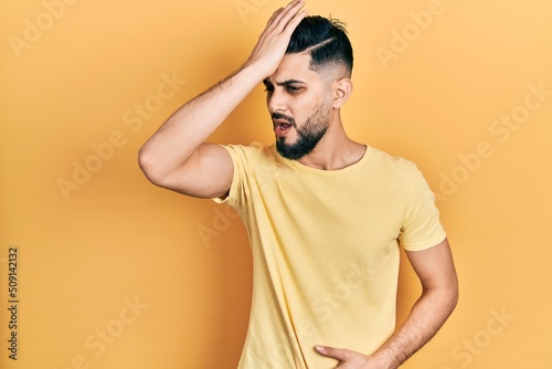 Handsome man with beard wearing casual yellow t shirt surprised with hand on head for mistake, remember error. forgot, bad memory concept. © Krakenimages.com
