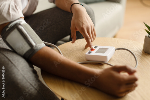 Cropped view of millennial black man sitting on couch at home, checking blood pressure, using modern tonometer © Prostock-studio