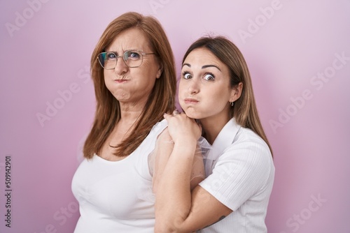 Hispanic mother and daughter wearing casual white t shirt puffing cheeks with funny face. mouth inflated with air, catching air.