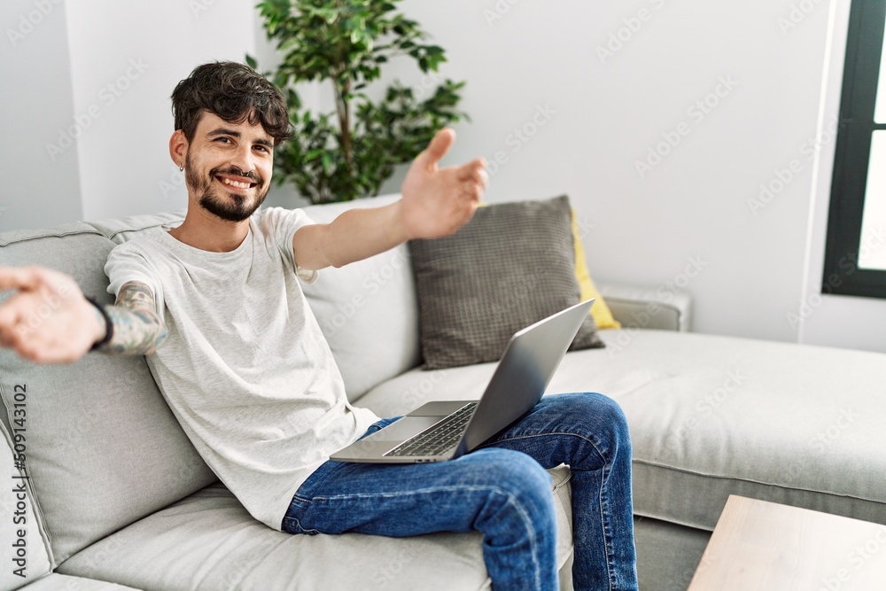 Hispanic man with beard sitting on the sofa looking at the camera smiling with open arms for hug. cheerful expression embracing happiness. Hispanic man with beard sitting on the sofa looking at the camera smiling with open arms for hug. cheerful expression embracing happiness.