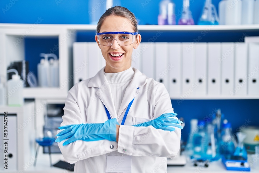 Young woman scientist smiling confident standing with arms crossed gesture at laboratory