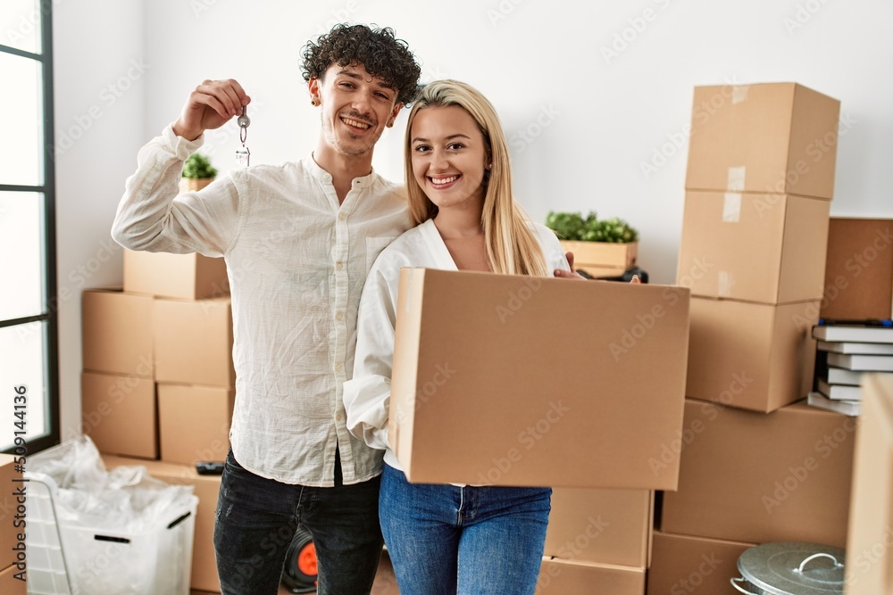 Young beautiful couple smiling happy holding cardboard box and key of new home. Young beautiful couple smiling happy holding cardboard box and key of new home.