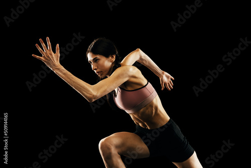 Studio shot of young muscular woman running isolated on black background. Sport, track-and-field athletics, competition and active lifestyle concept