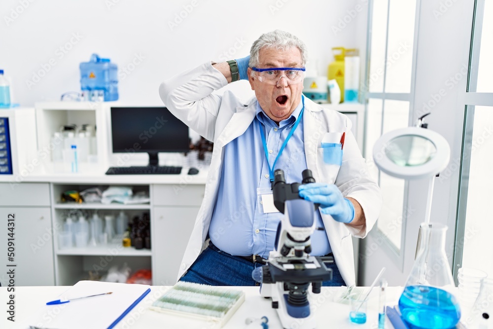 Senior caucasian man working at scientist laboratory crazy and scared with hands on head, afraid and surprised of shock with open mouth Senior caucasian man working at scientist laboratory crazy and scared with hands on head, afraid and surprised of shock with open mouth