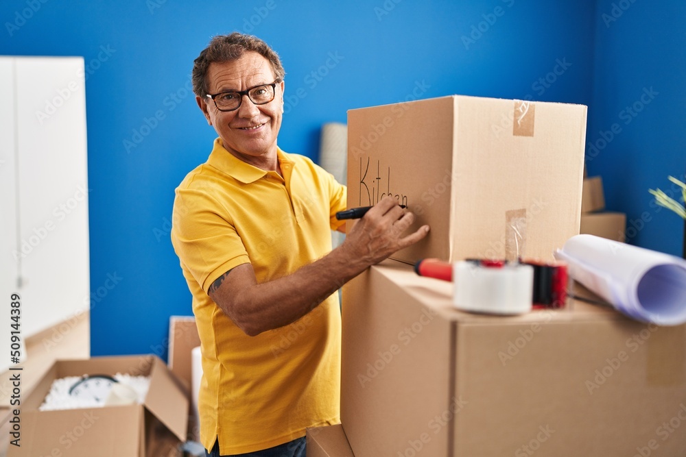 Middle age man smiing confident writing on package at new home Middle age man smiing confident writing on package at new home