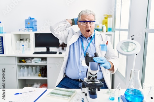 Senior caucasian man working at scientist laboratory crazy and scared with hands on head  afraid and surprised of shock with open mouth
