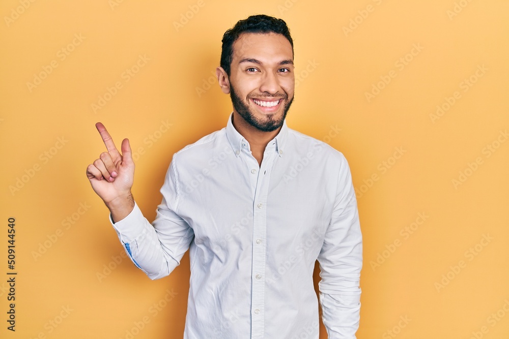Hispanic man with beard wearing business shirt with a big smile on face, pointing with hand and finger to the side looking at the camera. Hispanic man with beard wearing business shirt with a big smile on face, pointing with hand and finger to the side looking at the camera.