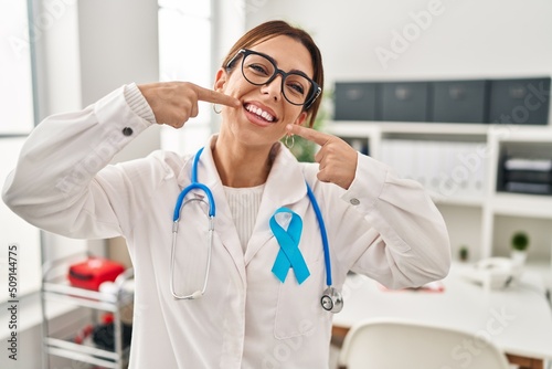 Young brunette doctor woman wearing stethoscope at the clinic smiling cheerful showing and pointing with fingers teeth and mouth. dental health concept.