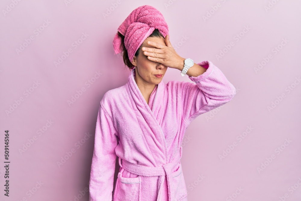 Young blonde woman wearing shower towel cap and bathrobe covering eyes with hand, looking serious and sad. sightless, hiding and rejection concept Young blonde woman wearing shower towel cap and bathrobe covering eyes with hand, looking serious and sad. sightless, hiding and rejection concept