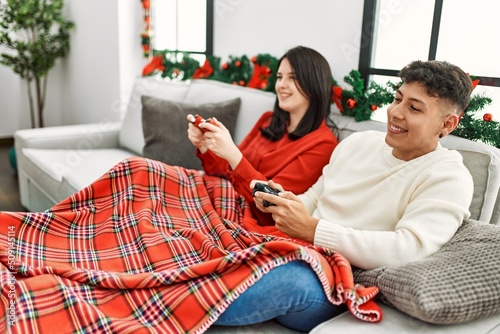 Young hispanic couple smiling happy sitting on the sofa playing video game at home.