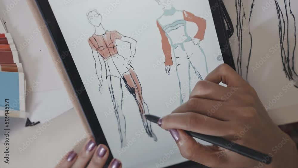 Top down close up shot of hands of African American female designer drawing fashion sketch on paper