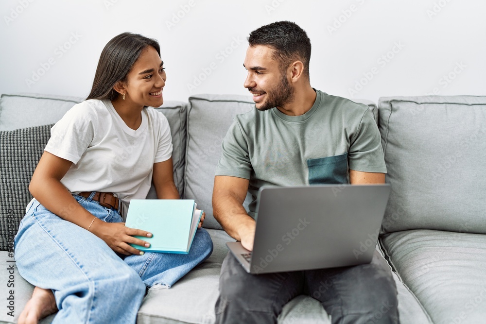 Young latin couple using laptop and reading book at home. Young latin couple using laptop and reading book at home.