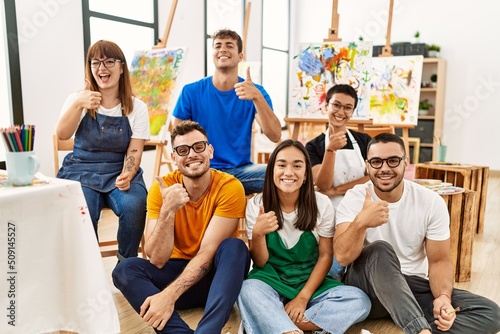 Group of people sitting at art studio smiling happy and positive, thumb up doing excellent and approval sign