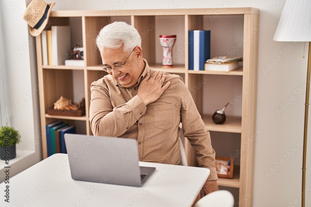Senior man using laptop suffering for shoulder pain at home